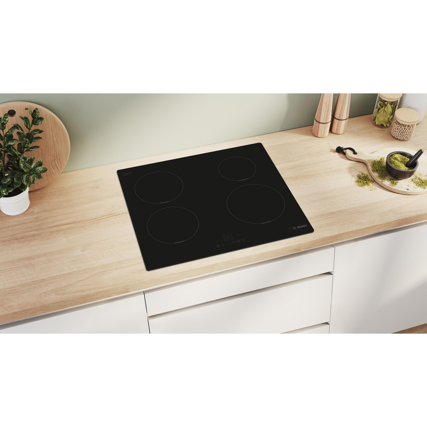 Piano cottura nero con quattro fuochi su un piano di lavoro in legno. Ambiente cucina con elementi verdi e bianchi.