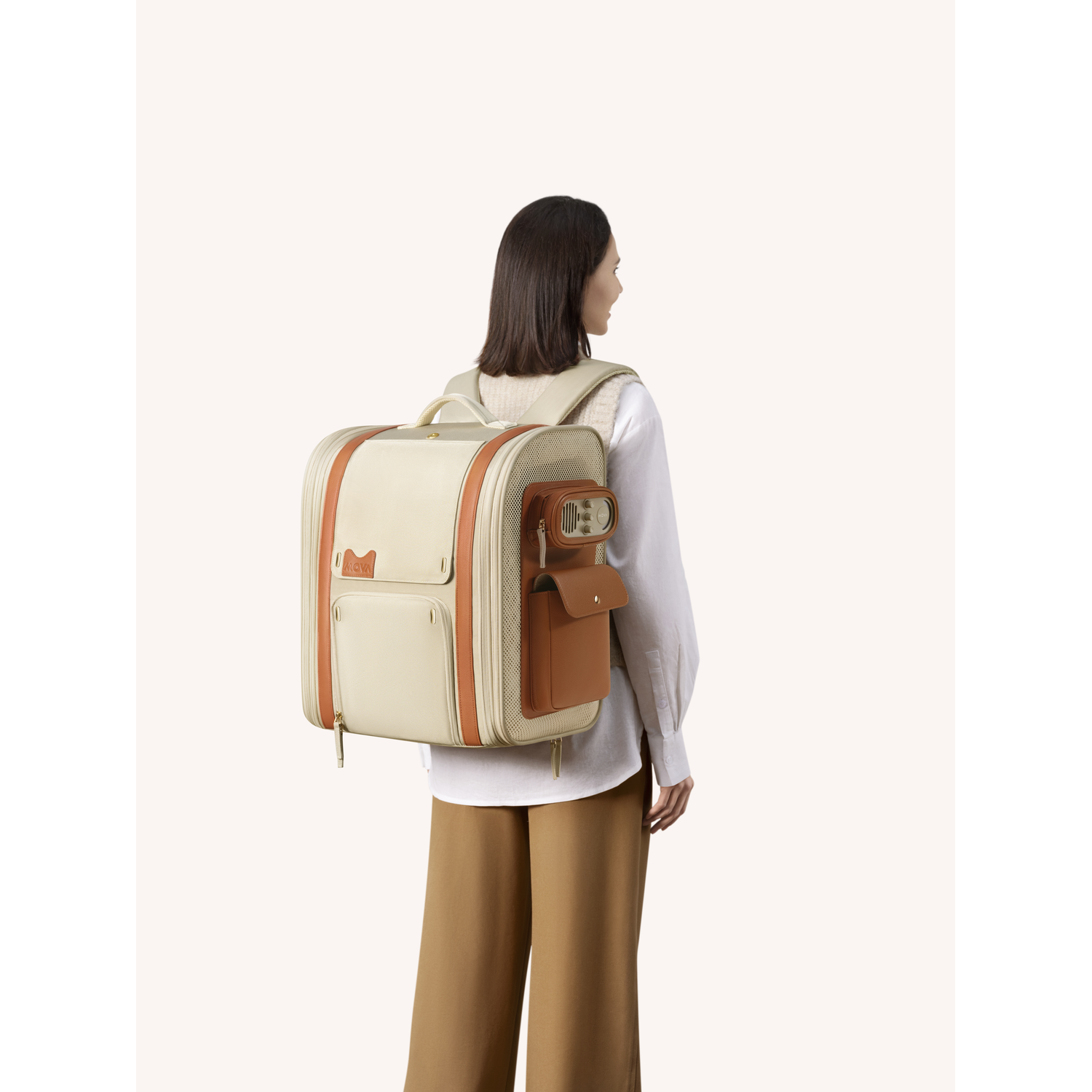 Woman with backpack. Beige and tan backpack on her back. She wears white shirt and brown pants, looking right.