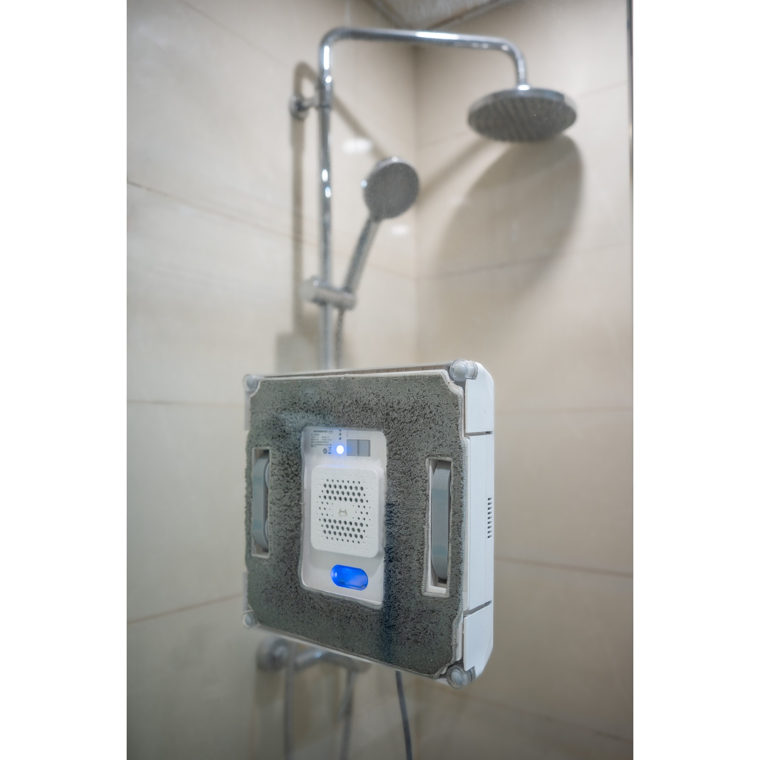 Robot pulisci vetri su vetro. Soffione doccia e accessori visibili sullo sfondo. Interni luminosi.