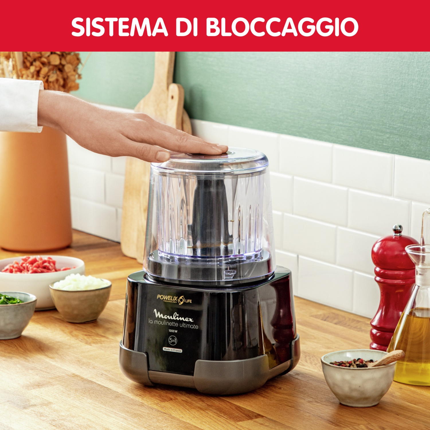Mano tocca un robot da cucina nero. Ingredienti in ciotole su un bancone di legno, spezie.