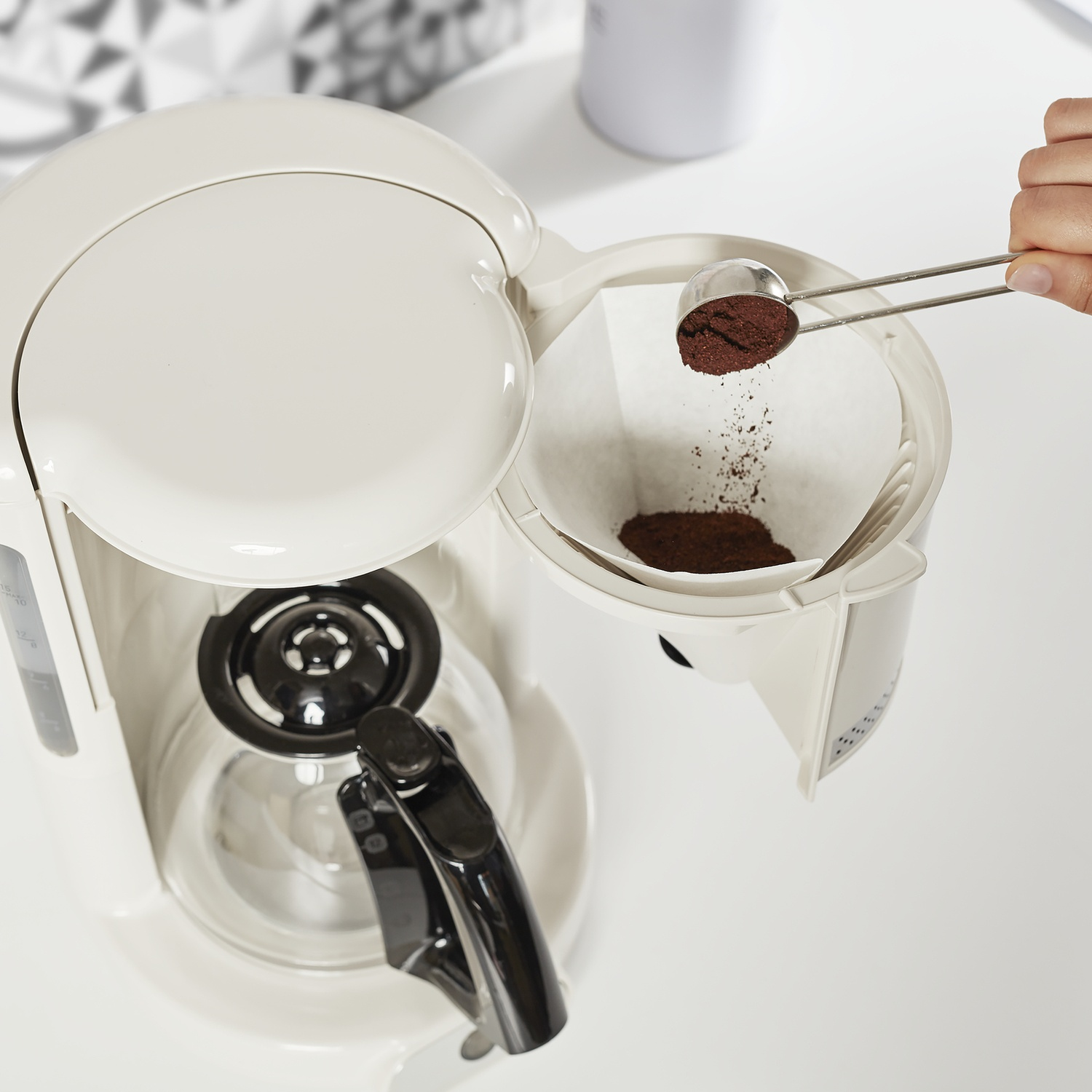 Una persona versa caffè macinato in un filtro in una caffettiera bianca, su una superficie bianca.