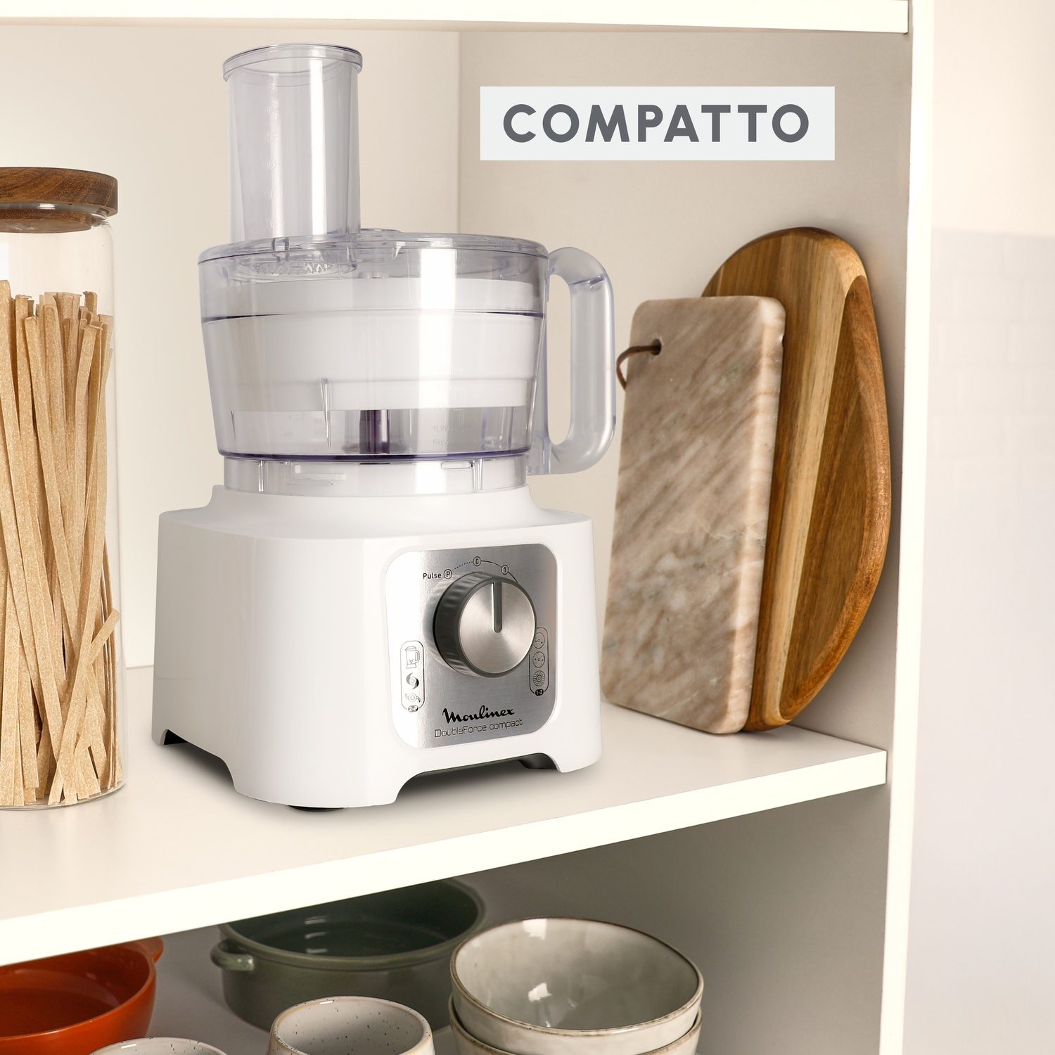 Robot da cucina Moulinex bianco su un ripiano con taglieri in legno e pasta in un barattolo.