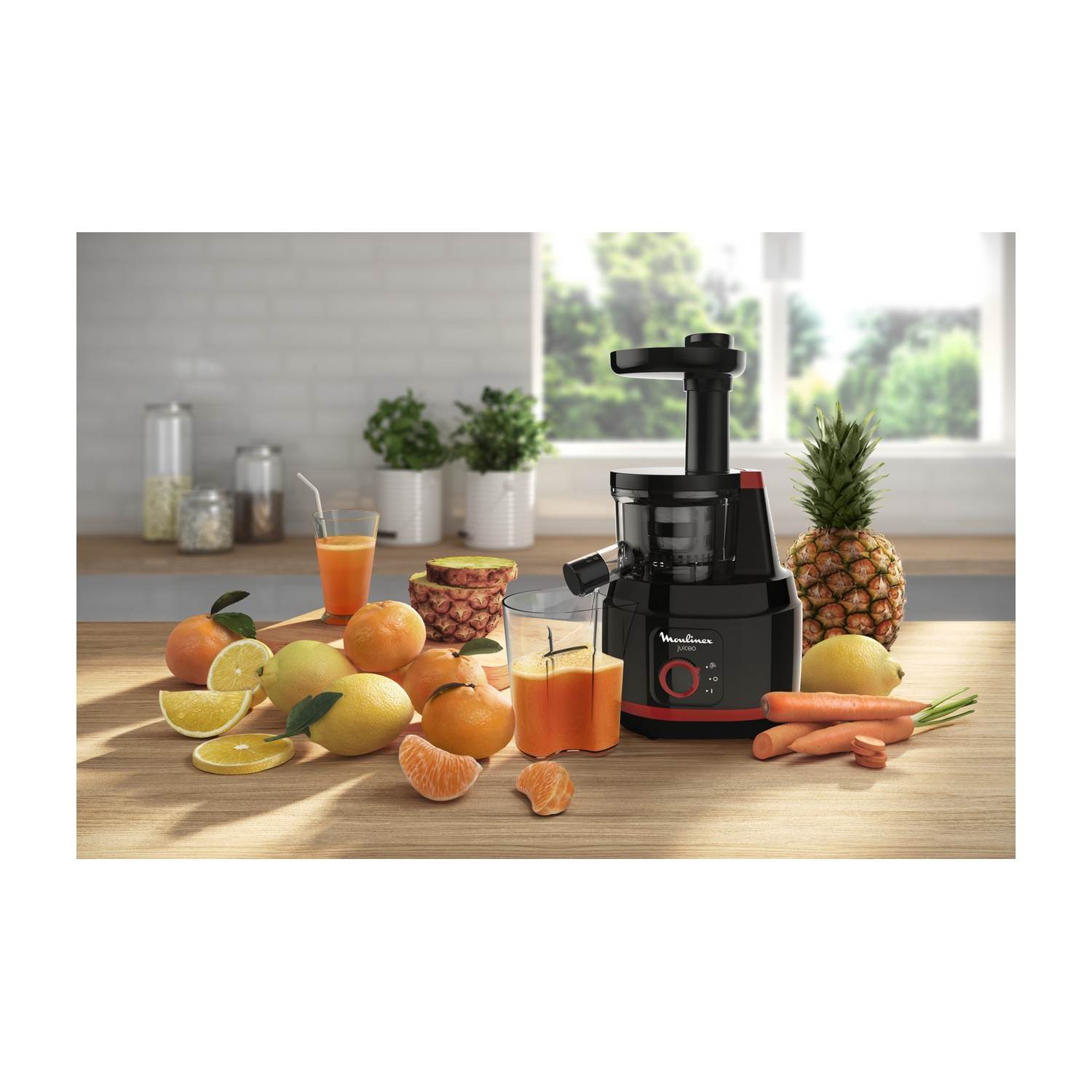 Un estrattore di succo con frutta e verdura su un tavolo di legno. Ci sono bicchieri con succo e una finestra sullo sfondo.
