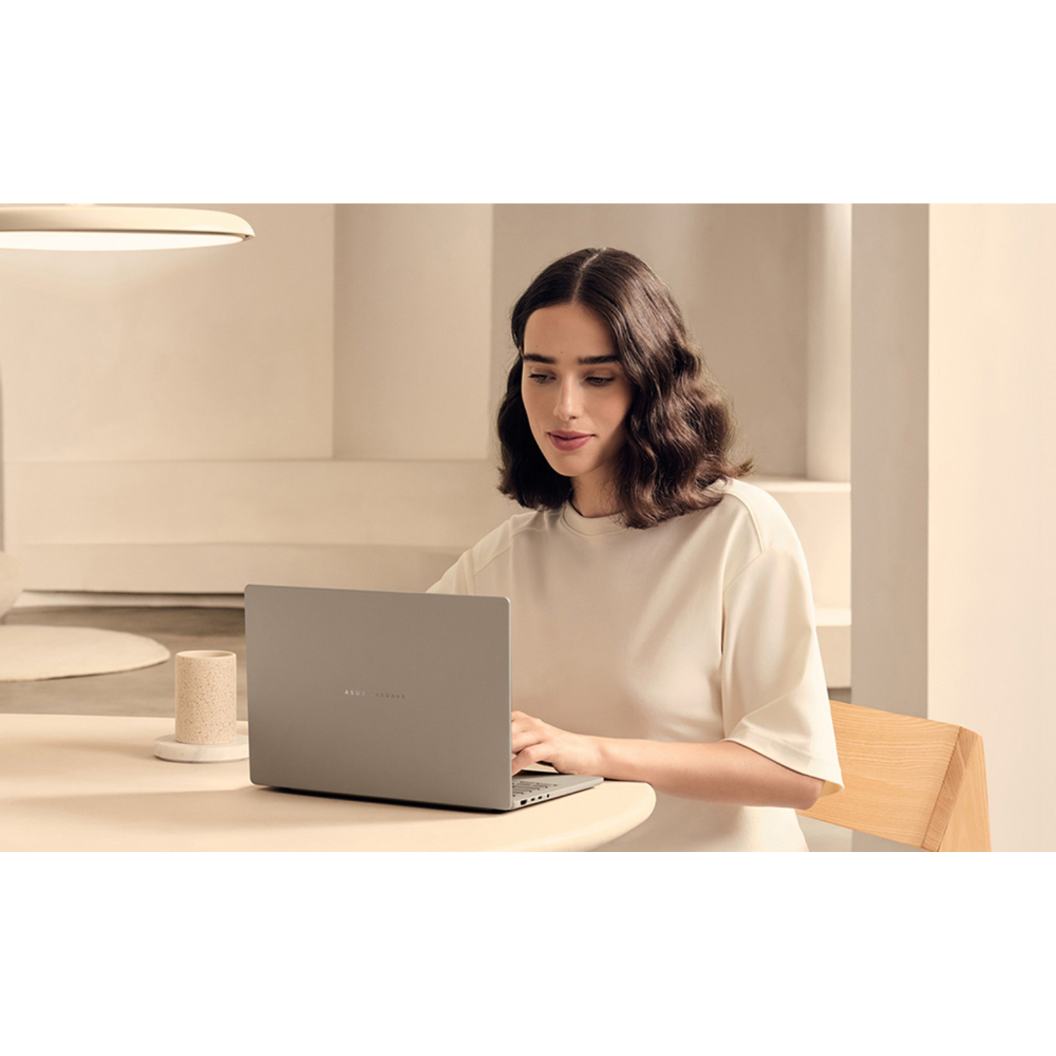 Woman with a laptop at a table. There is a cup and a light above.
