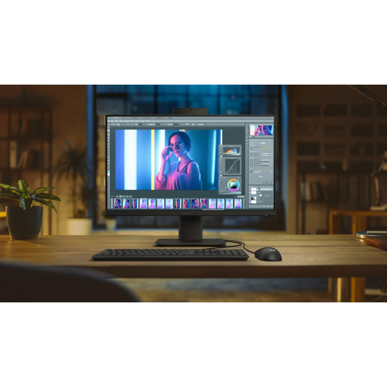 Een monitor toont een foto-bewerkingsinterface. Een toetsenbord, muis en plant staan op het bureau.