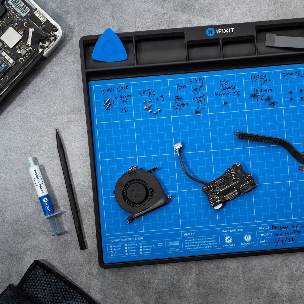 MacBook Air Teile auf einer blauen Rastermatte. Enthält Schrauben, Lüfter, Logic Board, Wärmeleitpaste und Werkzeuge.