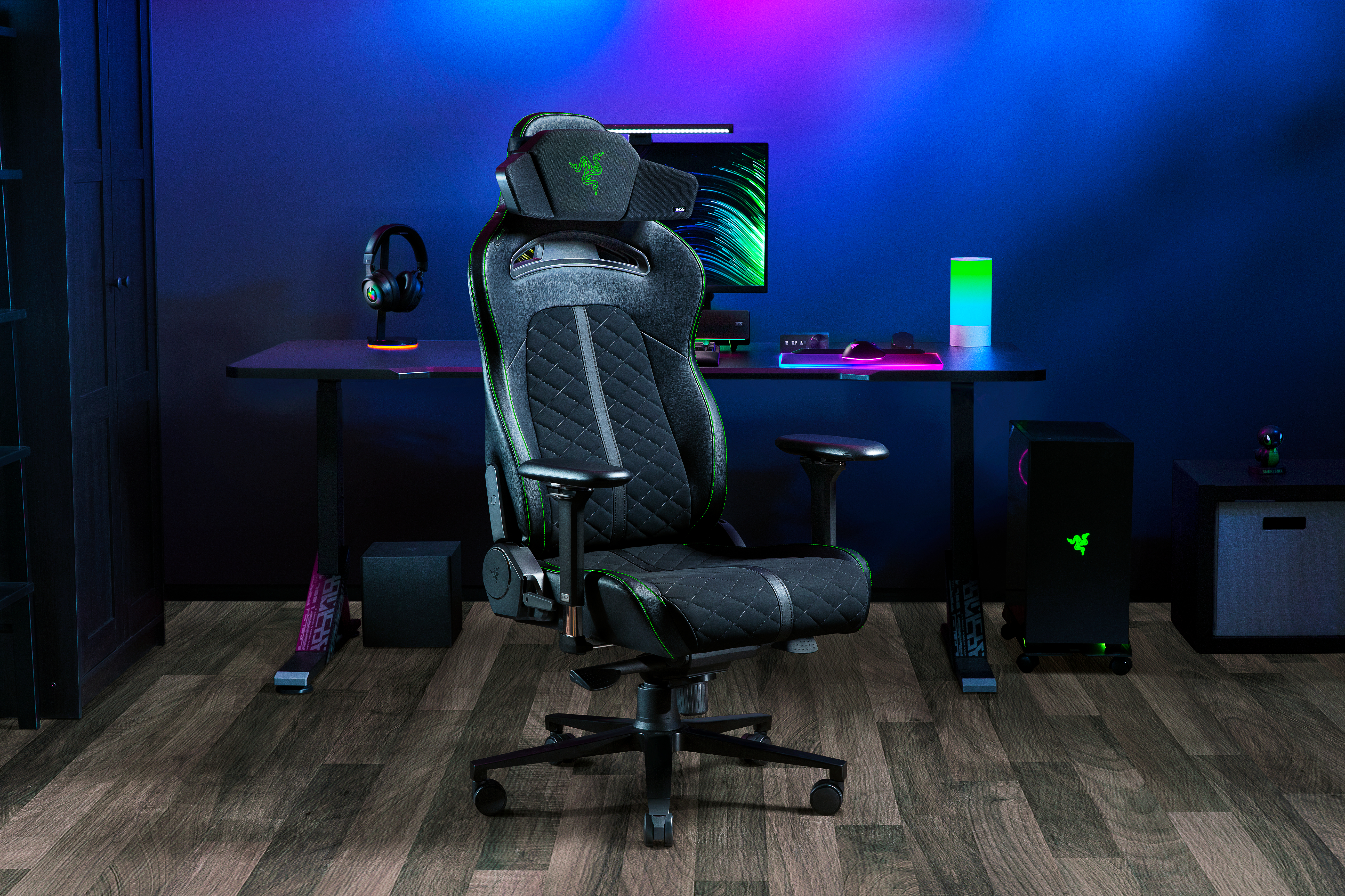 Gaming-Setup: Razer-Stuhl, Schreibtisch, Monitor, Kopfhörer, PC und Smart Speaker. Blaue und lila Beleuchtung. Holzfußboden.