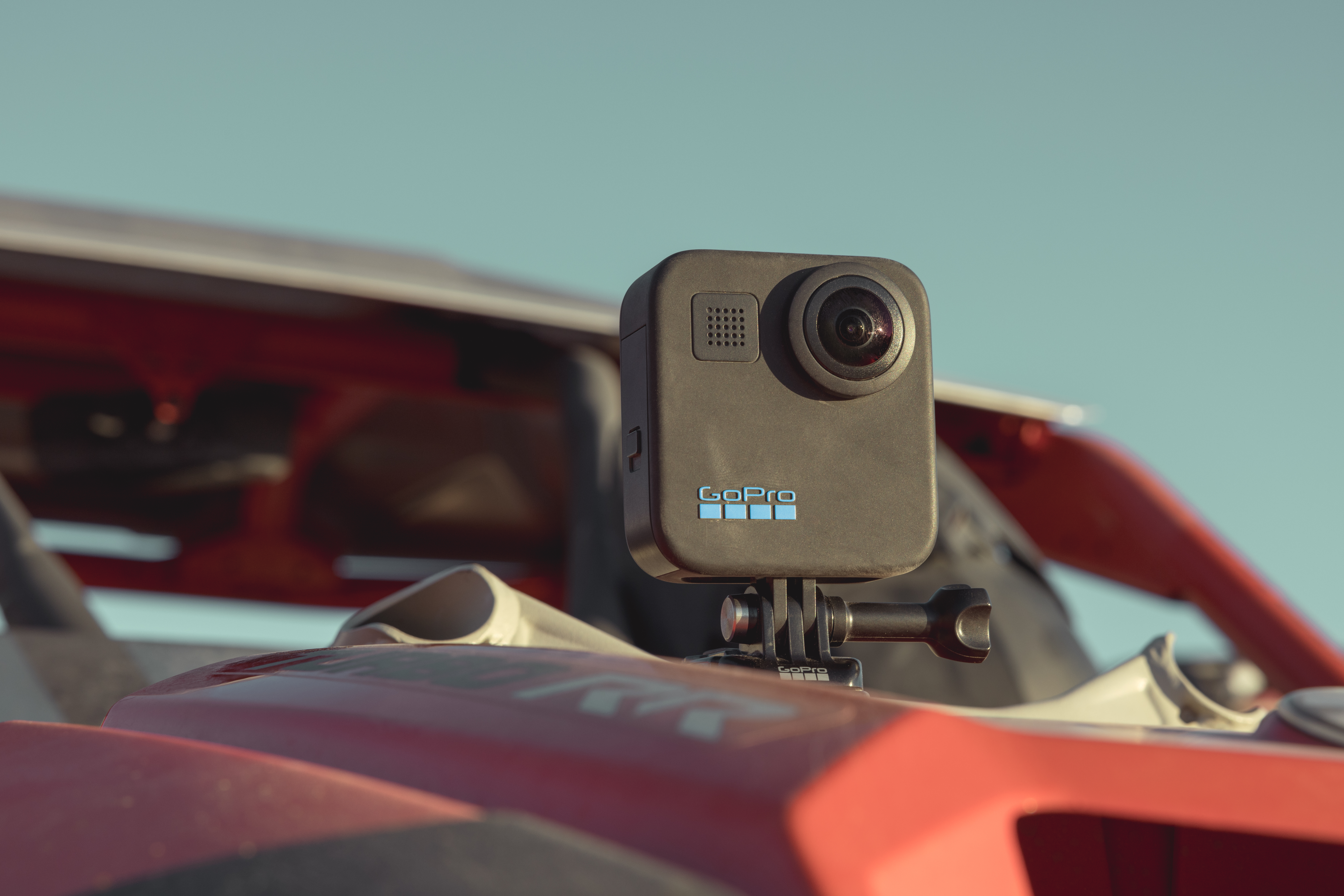Eine schwarze GoPro-Kamera ist auf einem roten Fahrzeug montiert. Der Hintergrund ist ein klarer blauer Himmel.
