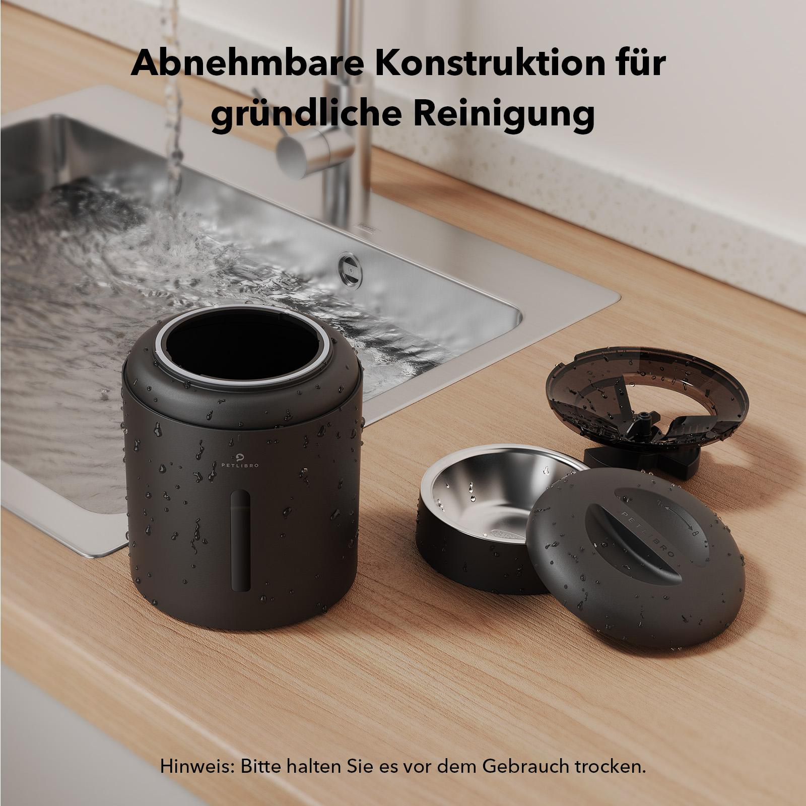 Ein schwarzer, zerlegter Futterautomat mit Wassertropfen, in der Nähe eines Waschbeckens. Teile umfassen eine Basis, Schüssel und Deckel.