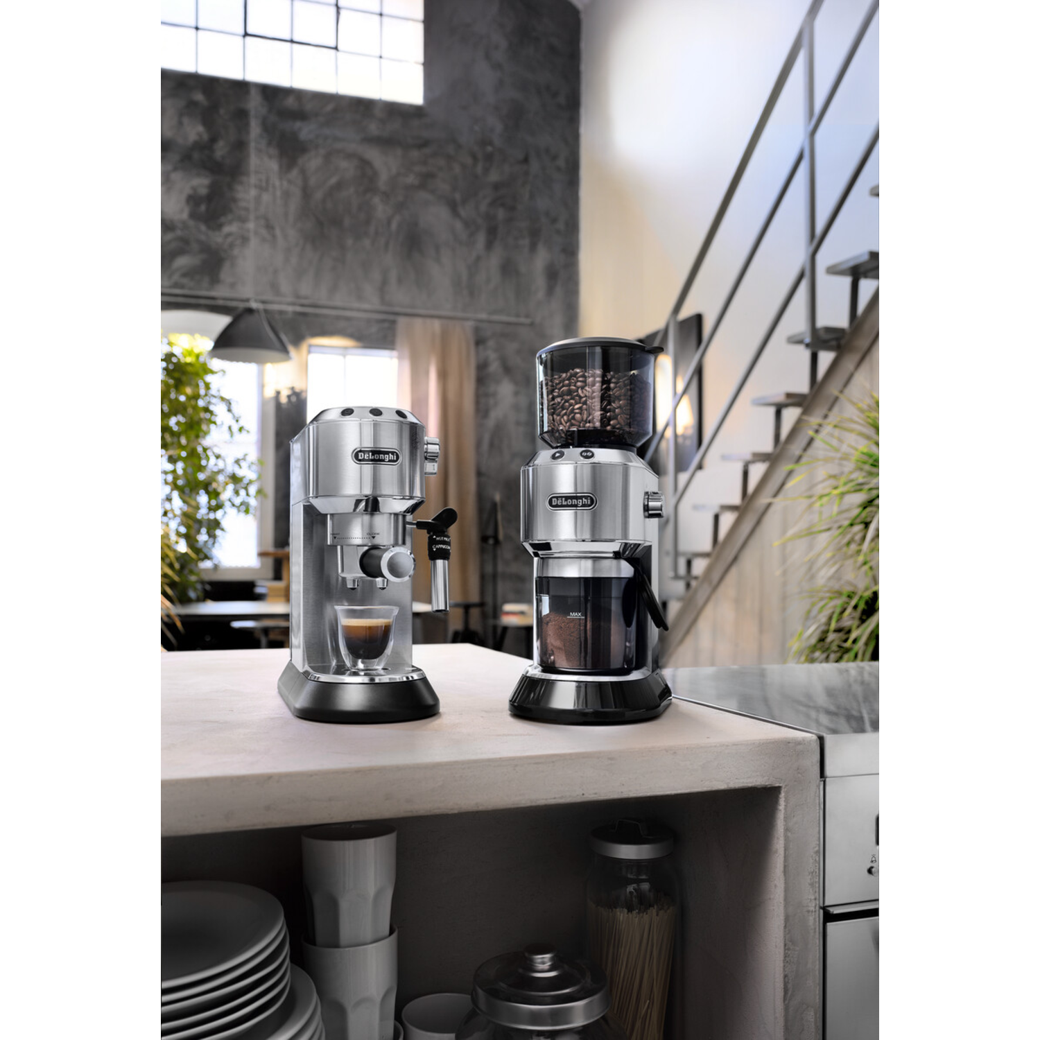 Twee DeLonghi espressomachines op een aanrecht. Eén zet koffie. Op de achtergrond zijn een trap en een raam te zien.