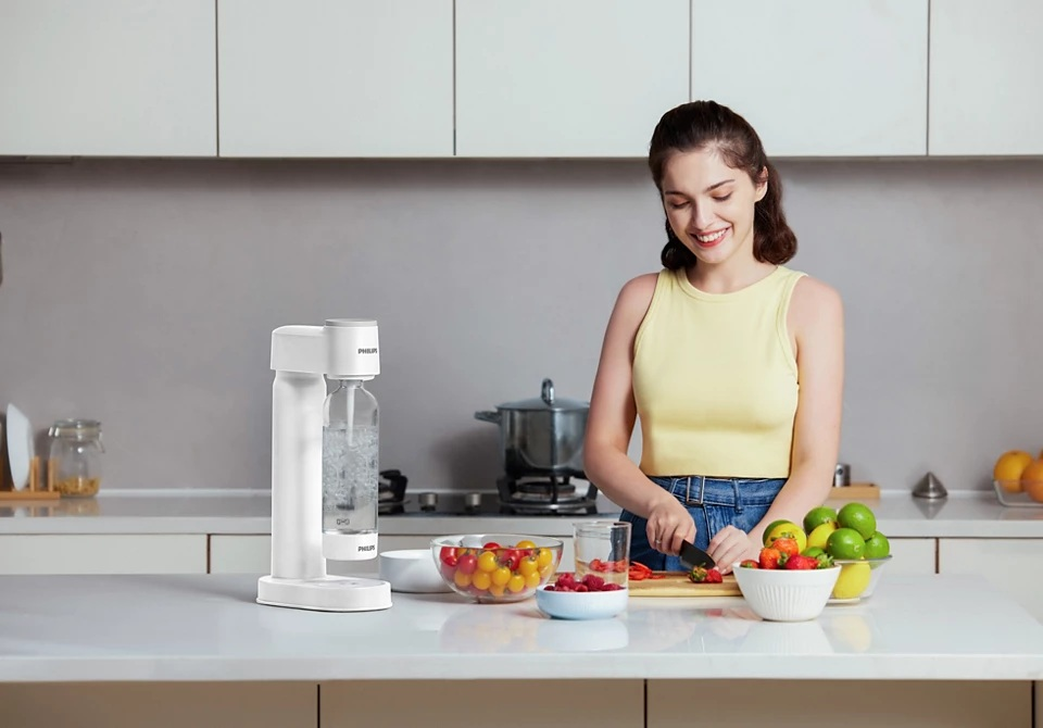 Kobieta kroi warzywa w kuchni, na blacie stoi urządzenie do produkcji sody.