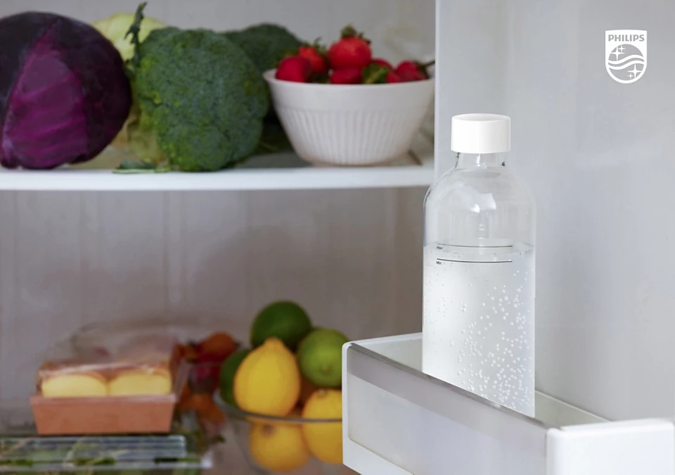 Butelka wody gazowanej w lodówce z owocami i warzywami.