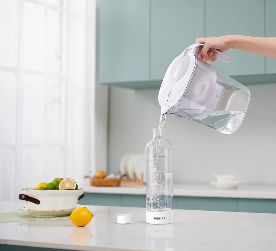 Osoba wlewa wodę z białego filtra Philips do butelki. Tło kuchni.