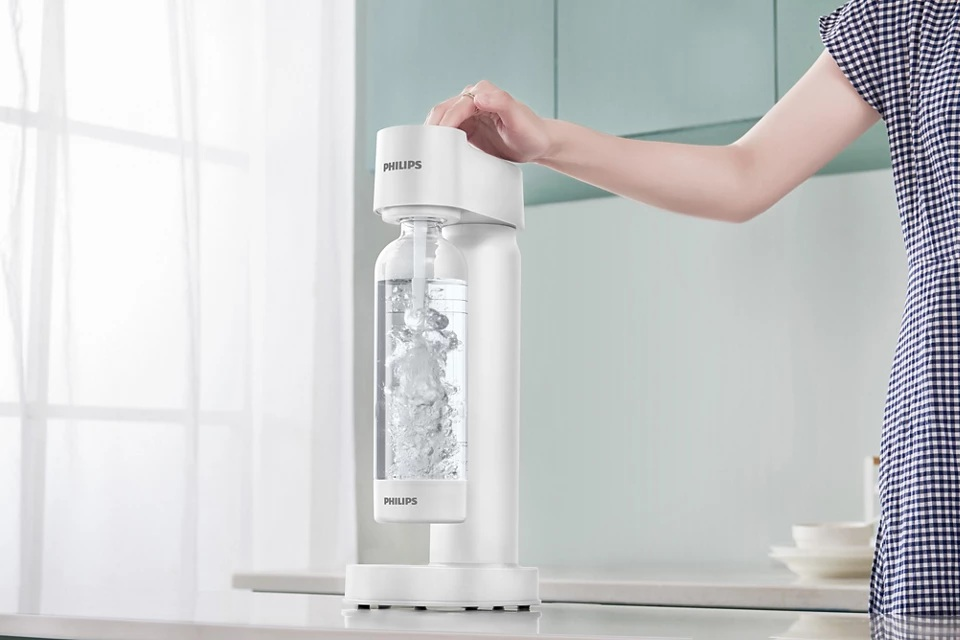 Osoba obsługuje biały system wodny Philips. Butelka w środku. Tło kuchni.