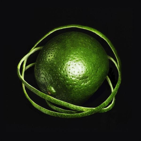Eine grüne Limette, umgeben von einer Spirale ihrer Schale, auf schwarzem Hintergrund.