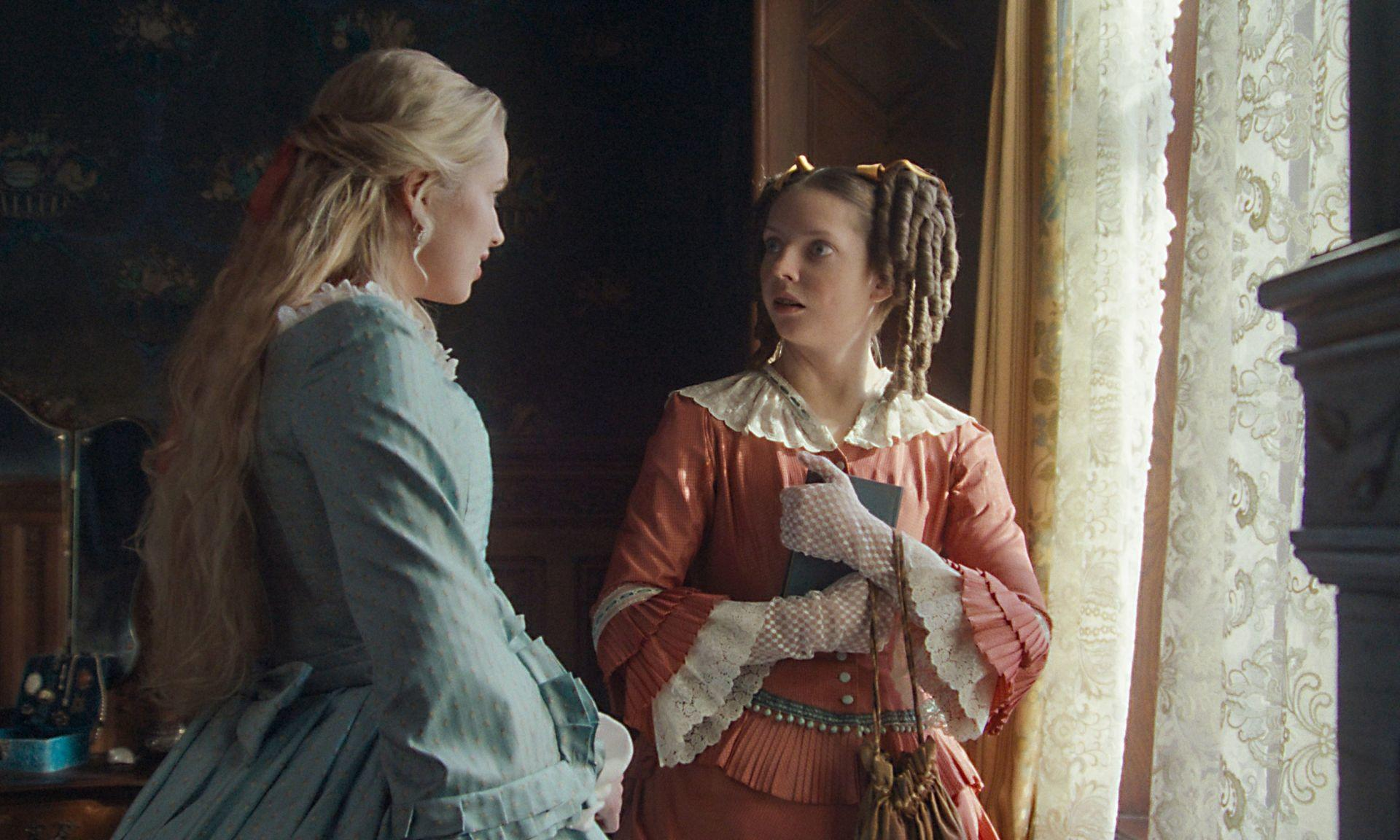 Zwei Frauen in historischen Kleidern unterhalten sich. Eine hält ein Buch, die andere hat aufwendiges Haar.