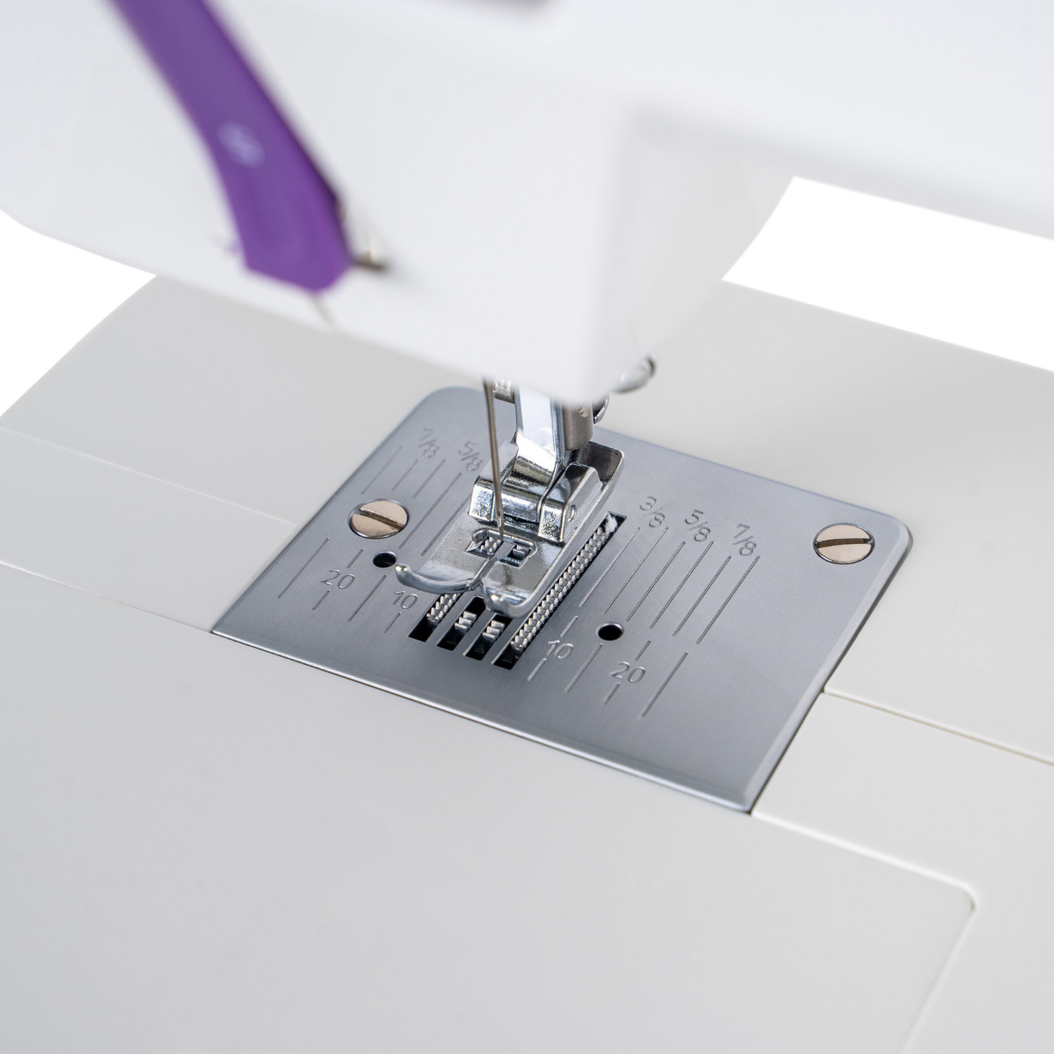 Zbliżenie na płytkę ściegową i igłę maszyny do szycia. Płytka ma na sobie miary.