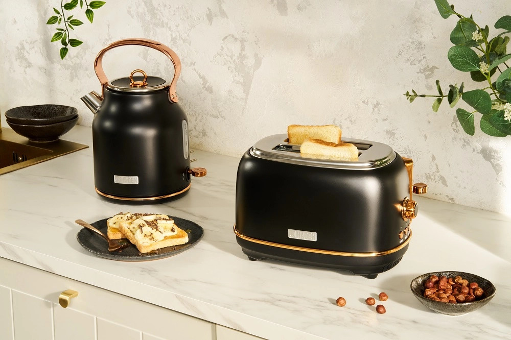 Scena kuchenna z czarnym tosterem i czajnikiem z miedzianymi akcentami, tostem, orzechami i talerzem.