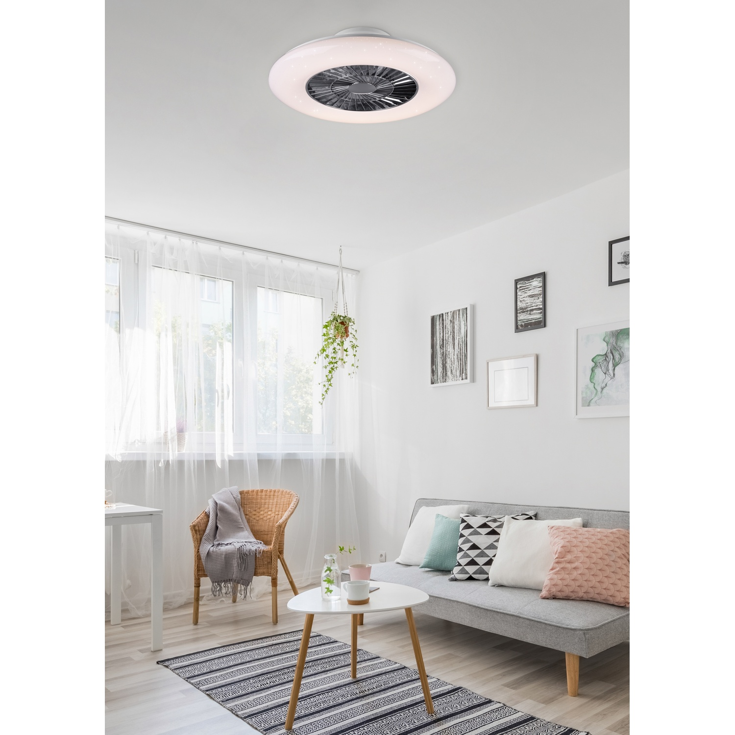 Scena della stanza: Ventilatore a soffitto bianco, pareti bianche e un divano grigio con cuscini e un tappeto.