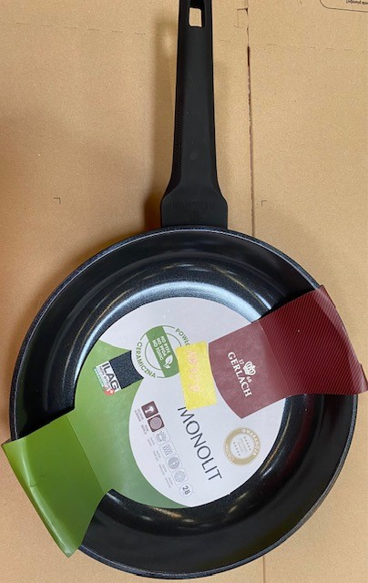 Czarna patelnia z długim uchwytem na brązowej powierzchni, z opakowaniem marki.