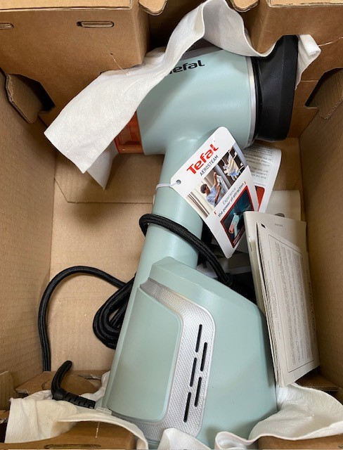 Żelazko parowe Tefal w pudełku. Żelazko jest jasnoniebieskie z czarnym przewodem i białymi akcesoriami.