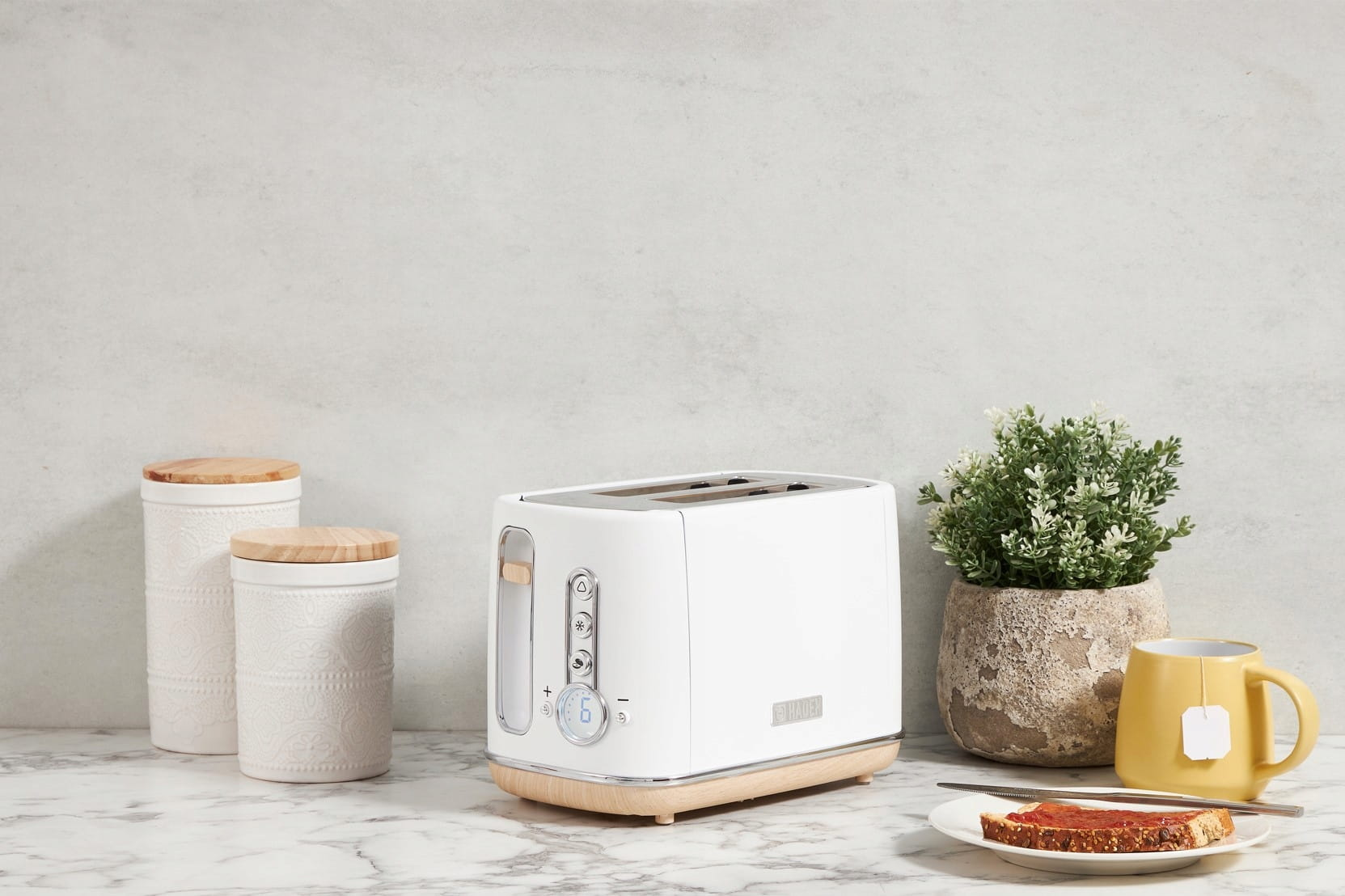 Biały toster z tostami, z talerzem jedzenia, jajkami i kwiatami na blacie.