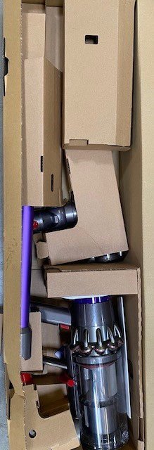 Otwarte pudełko odkurzacza Dyson. Widoczne są elementy, w tym fioletowa rura i srebrny silnik.