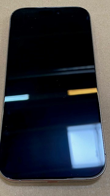 Czarny smartfon na jasnobrązowej powierzchni, pokazujący ekran, srebrną ramkę i odbicia światła.