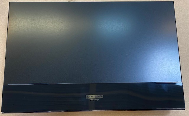 Czarny odtwarzacz Blu-ray z logo 'Ultra HD Blu-ray'. Metaliczne wykończenie. Jasne tło.