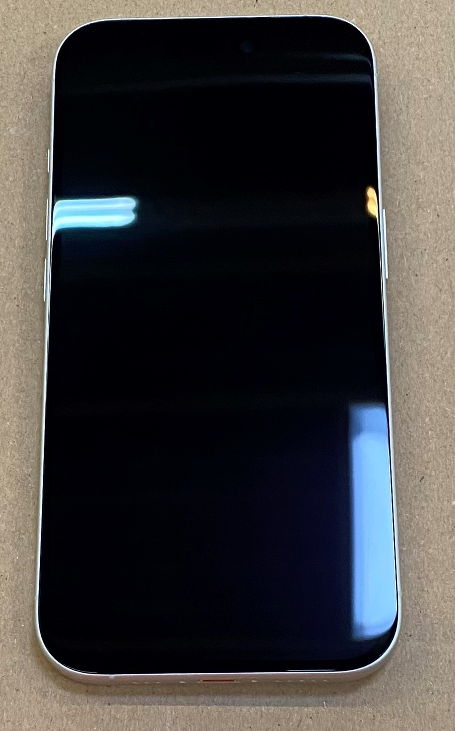 Czarny ekran telefonu na brązowej powierzchni, widoczna górna kamera.