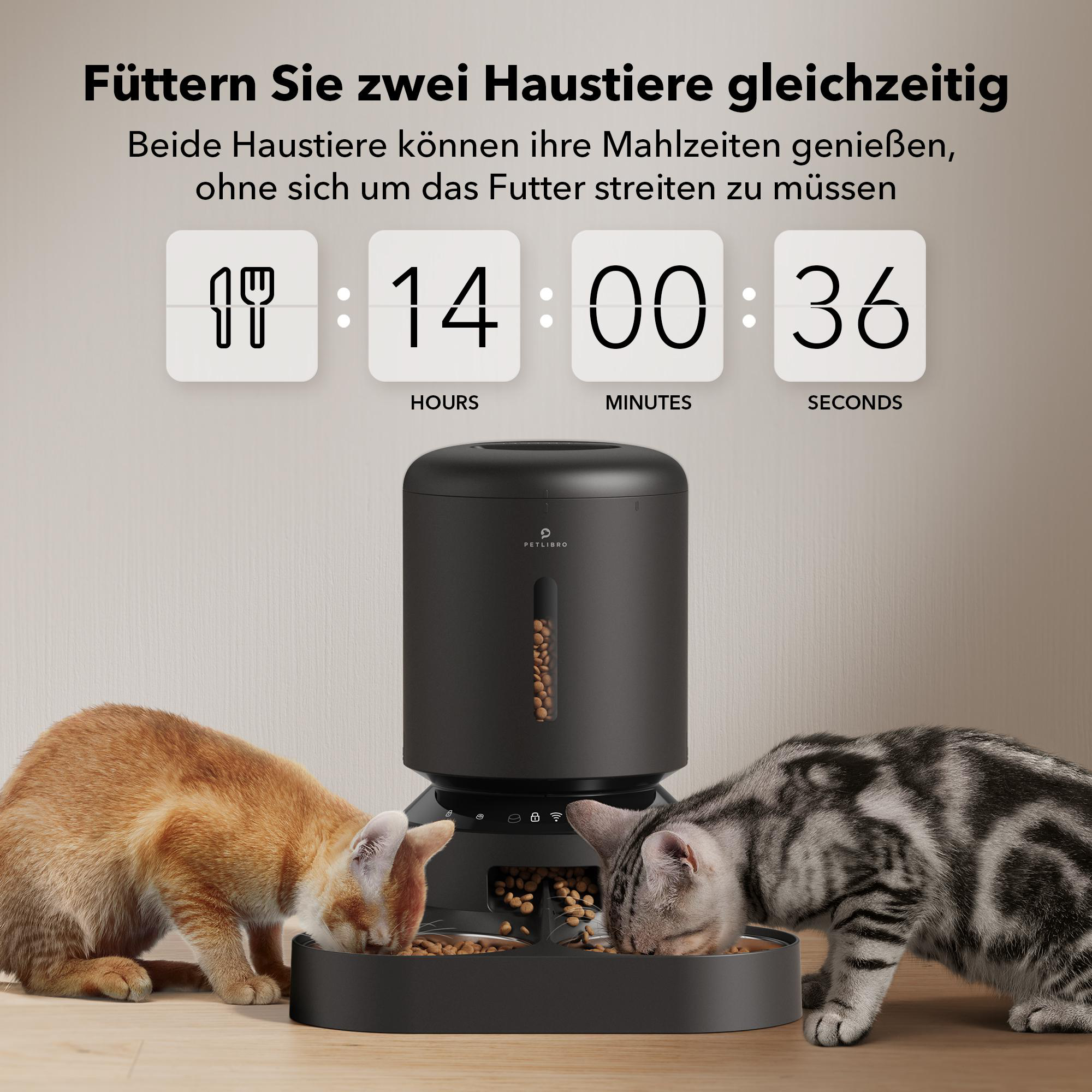 Zwei Katzen essen aus Futternäpfen neben einem automatischen Futterautomaten.