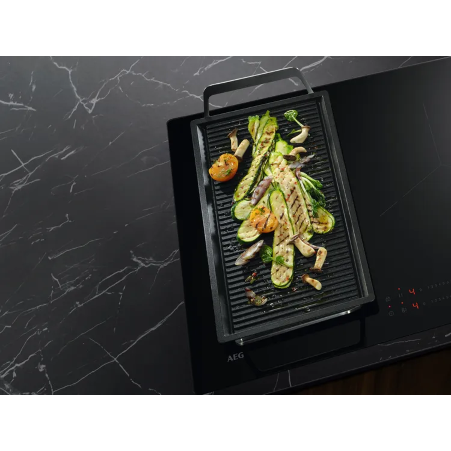 Grill pan with grilled vegetables on a black induction cooktop. Black marble countertop.