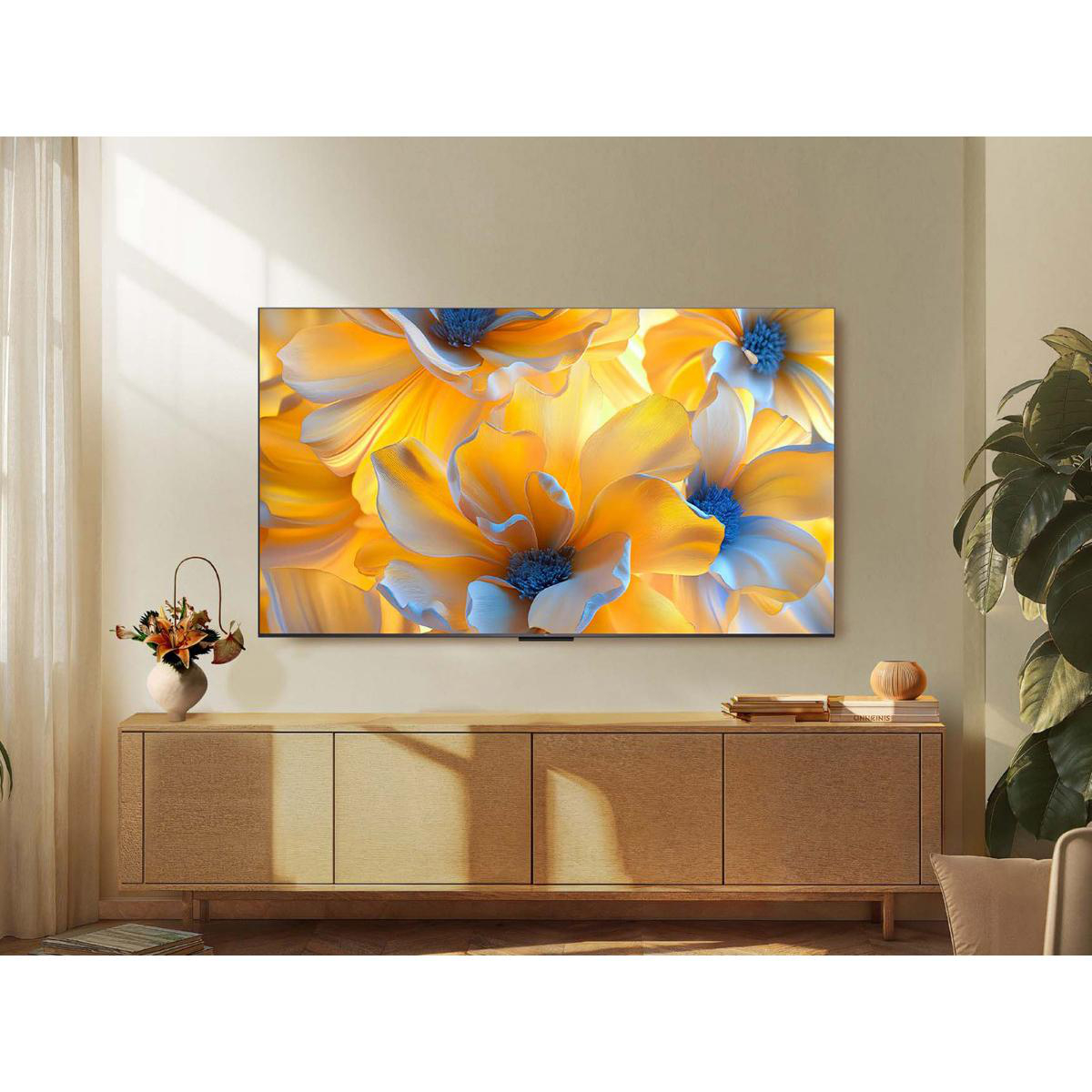 Ein großer Fernseher zeigt bunte Blumen. Er steht auf einem Holzschrank mit einer Pflanze.