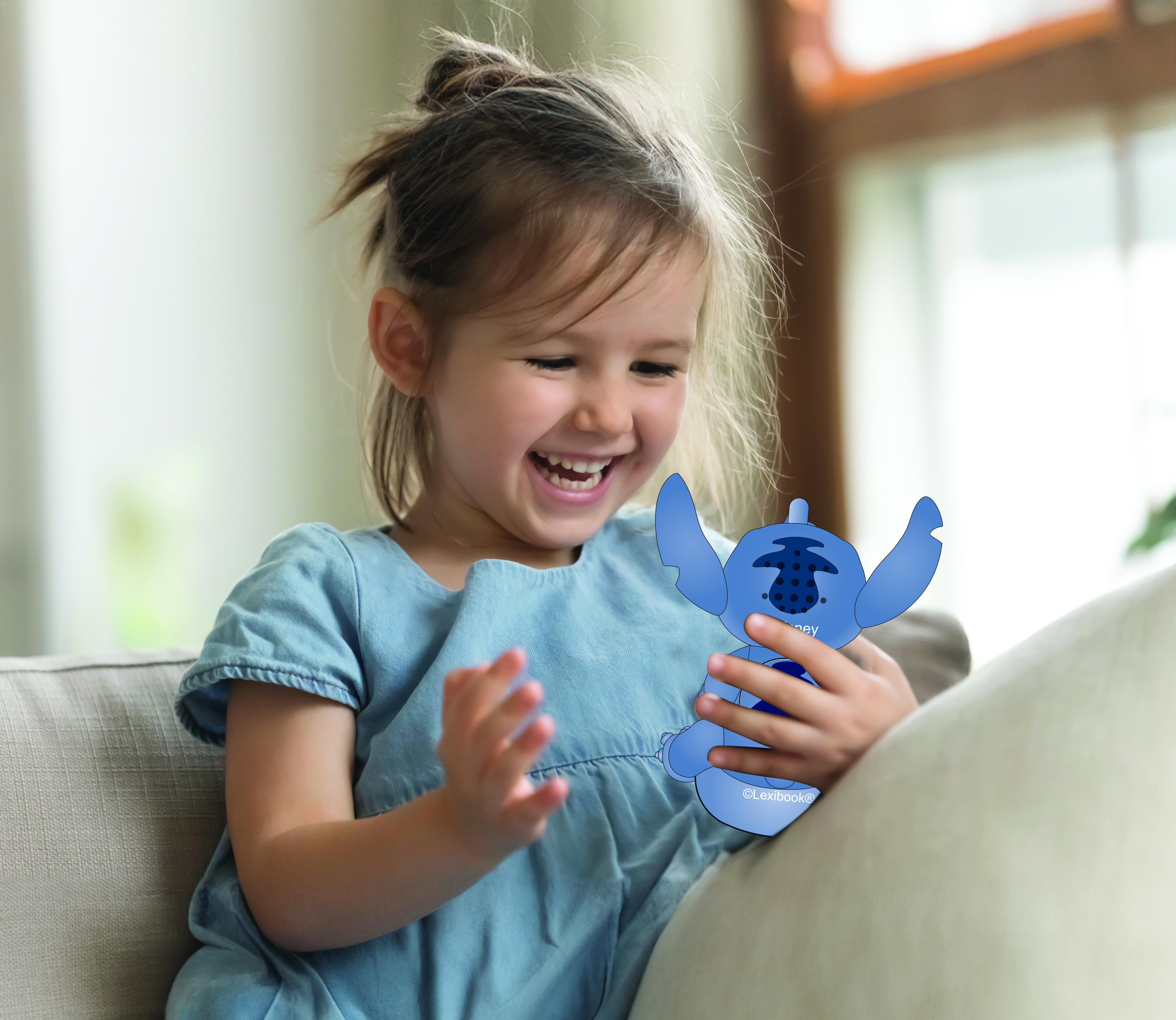 Ein Mädchen lächelt und hält ein Stitch-Spielzeug auf einem grauen Sofa.