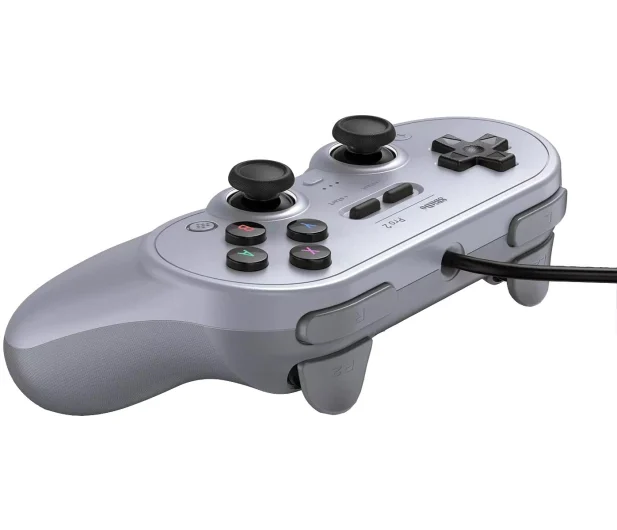 Srebrny kontroler 8BitDo Pro 2, widok z boku pod kątem. Widoczne przyciski, triggery i gałki analogowe.
