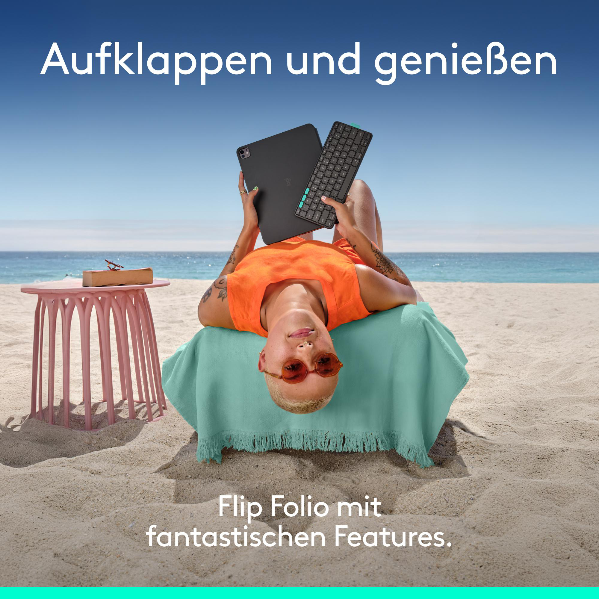 Eine Frau liegt auf einem Strandtuch mit einem iPad und einer Tastatur. Der Text 'Aufklappen und genießen' steht oben.