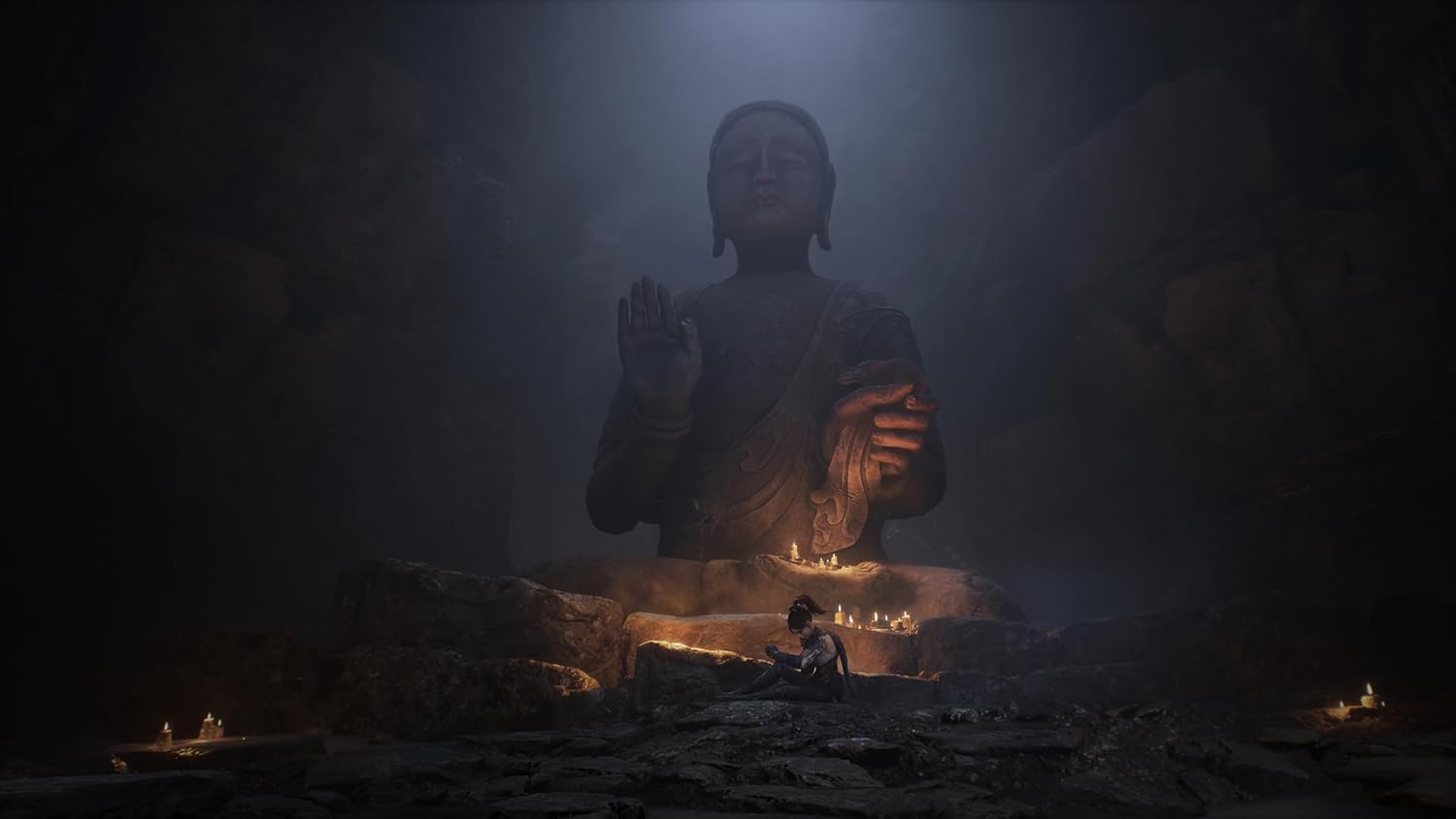 Una persona se sienta ante una estatua gigante de Buda, iluminada por velas, en un entorno de cueva.