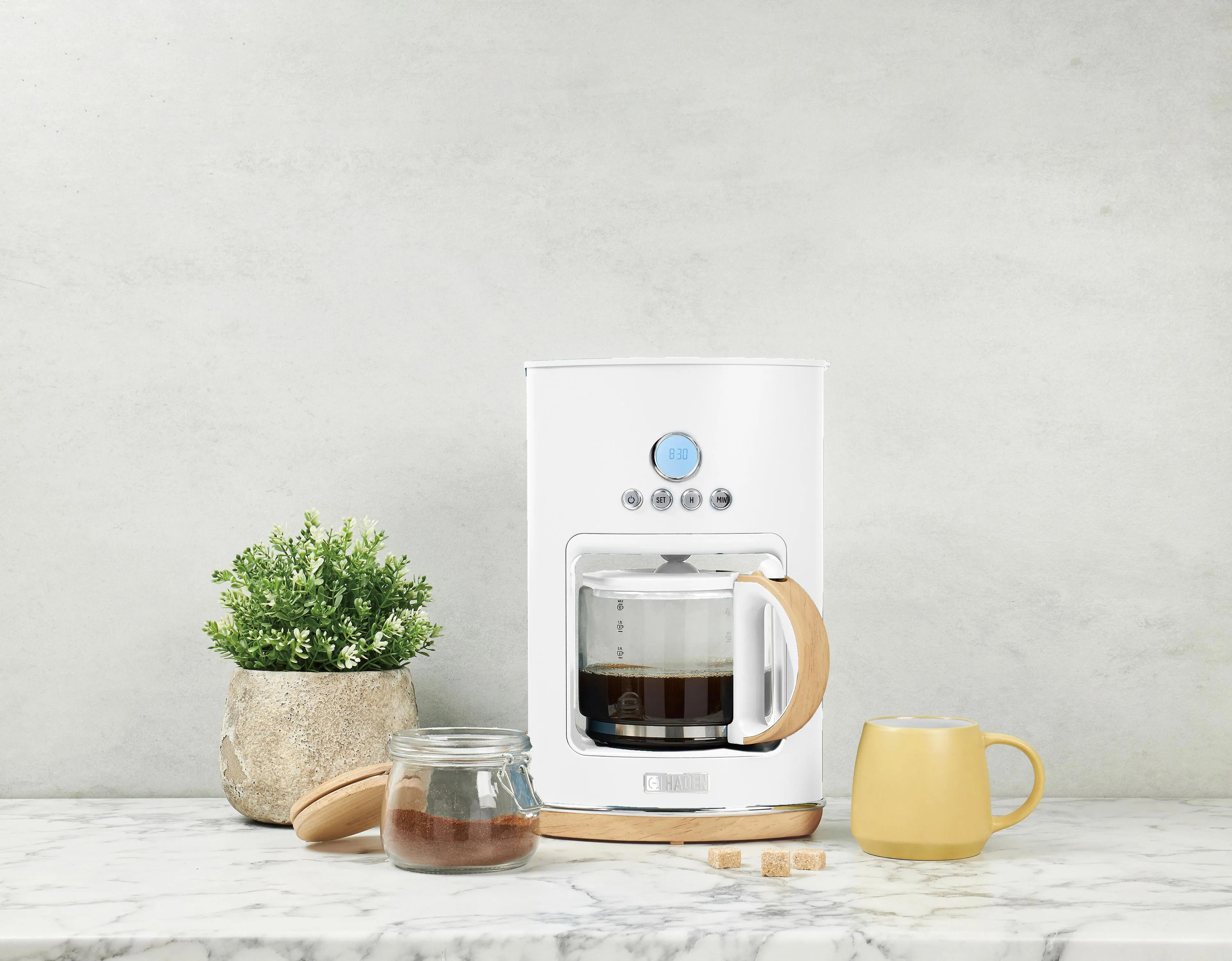 Ekspres do kawy i akcesoria. Kawa, rośliny, cukier i żółty kubek na marmurze.