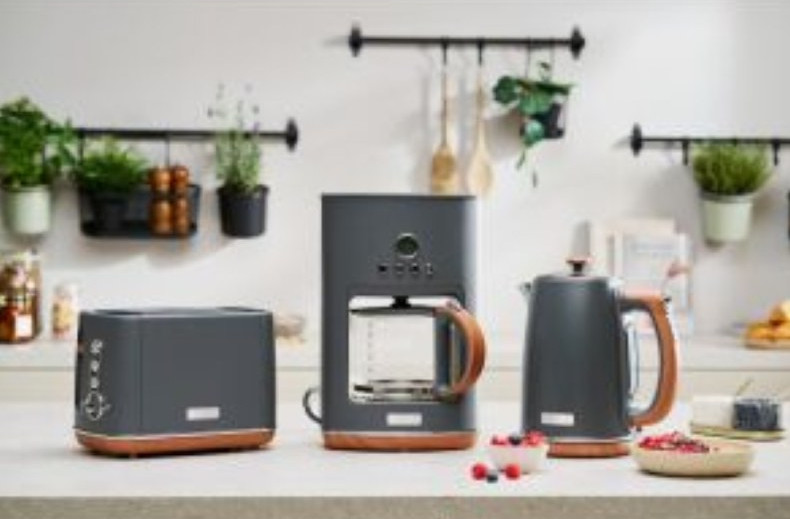 Urządzenia kuchenne: szary toster, ekspres do kawy i czajnik z drewnianymi akcentami. Na białym blacie.