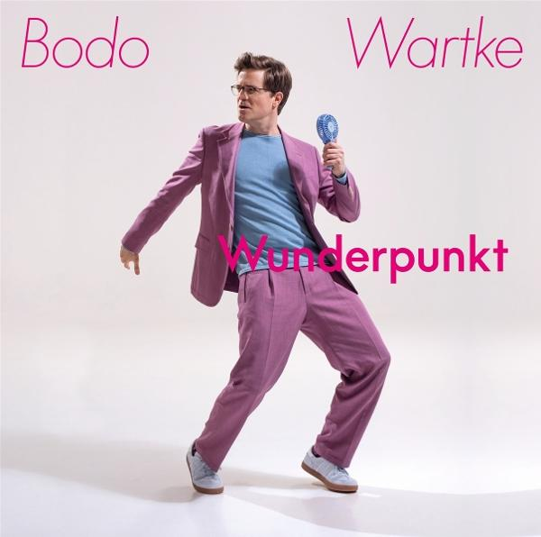 Mann im rosa Anzug mit blauem Fächer, Text 'Wunderpunkt' und Namen 'Bodo Wartke'.
