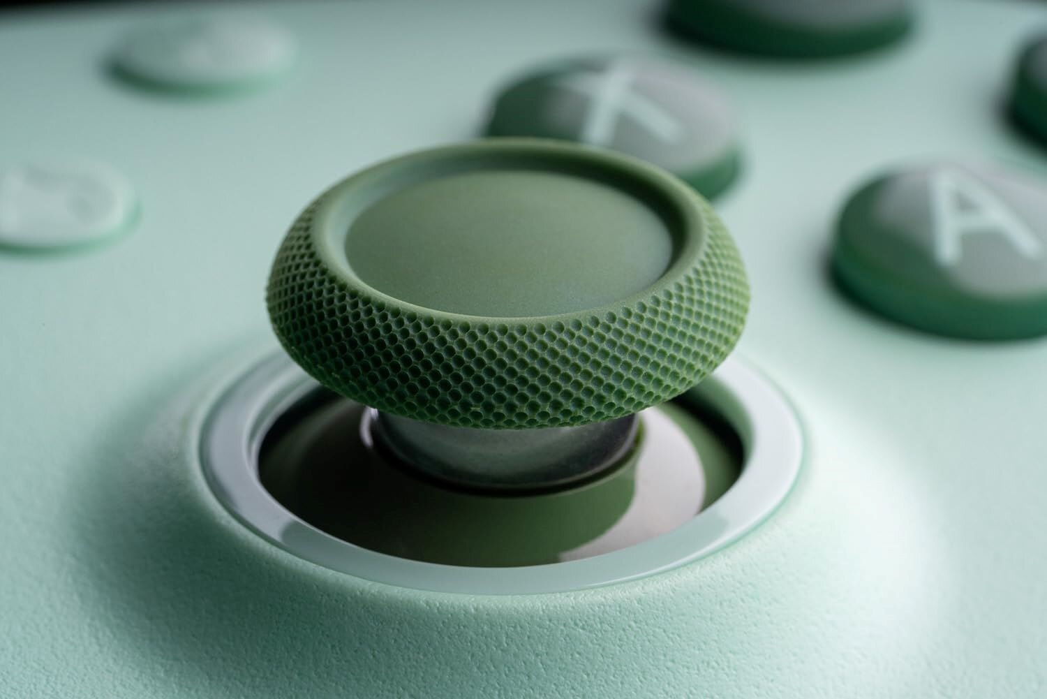 Zbliżenie zielonego joysticka na kontrolerze z przyciskami w tle.