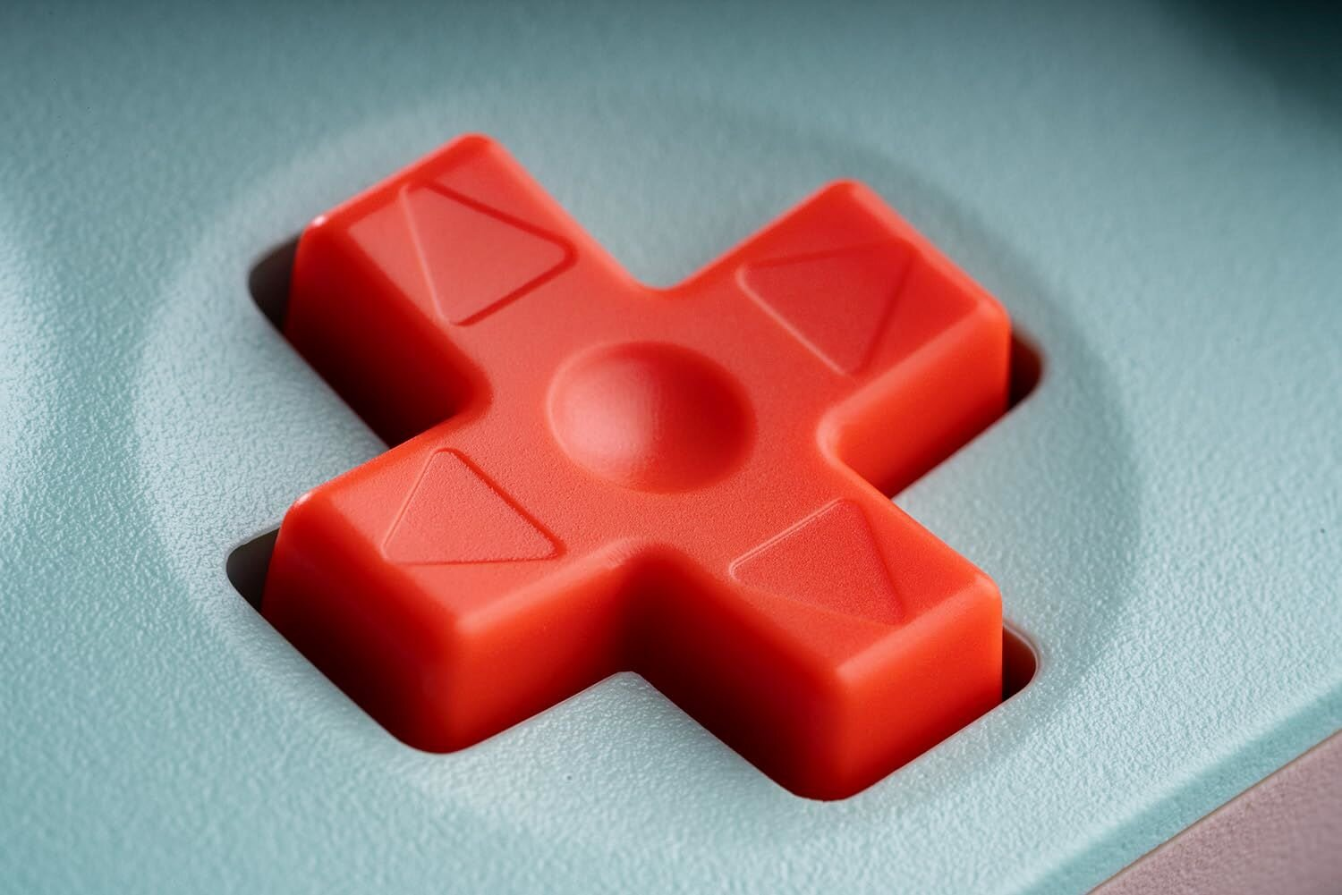 Zbliżenie koralowego przycisku D-pad. Miętowe tło.