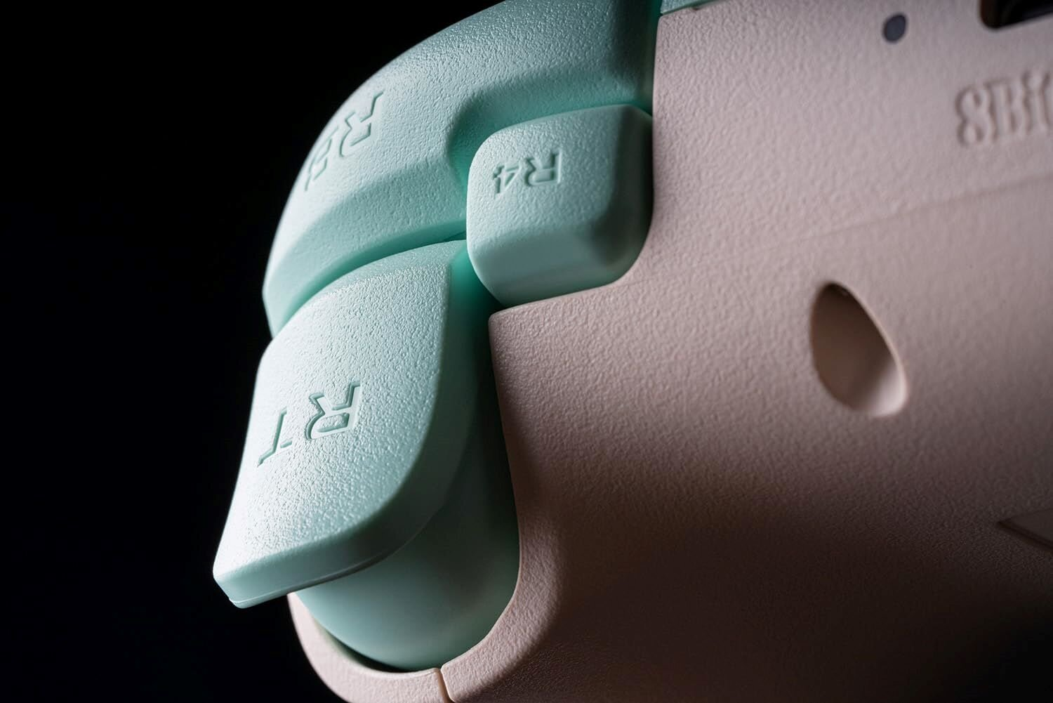 Zbliżenie boku kontrolera ze spustami. Miętowy i różowy kolor. Czarne tło.