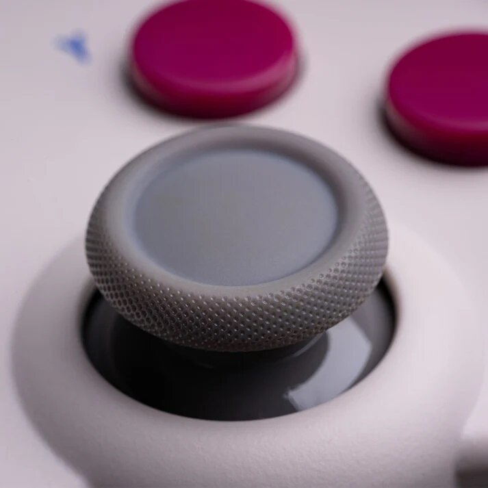 Zbliżenie szarego joysticka z białym kontrolerem i fioletowymi przyciskami.
