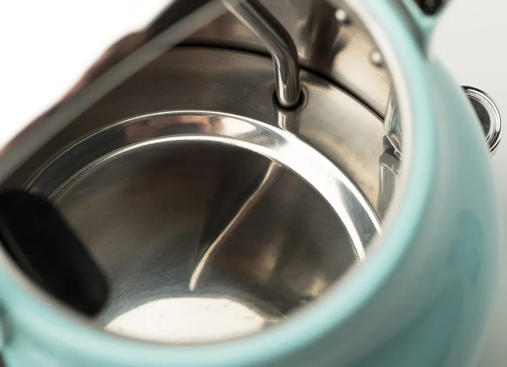 Widok od wewnątrz jasnoniebieskiego czajnika. Błyszczące, metaliczne wnętrze. Białe tło.