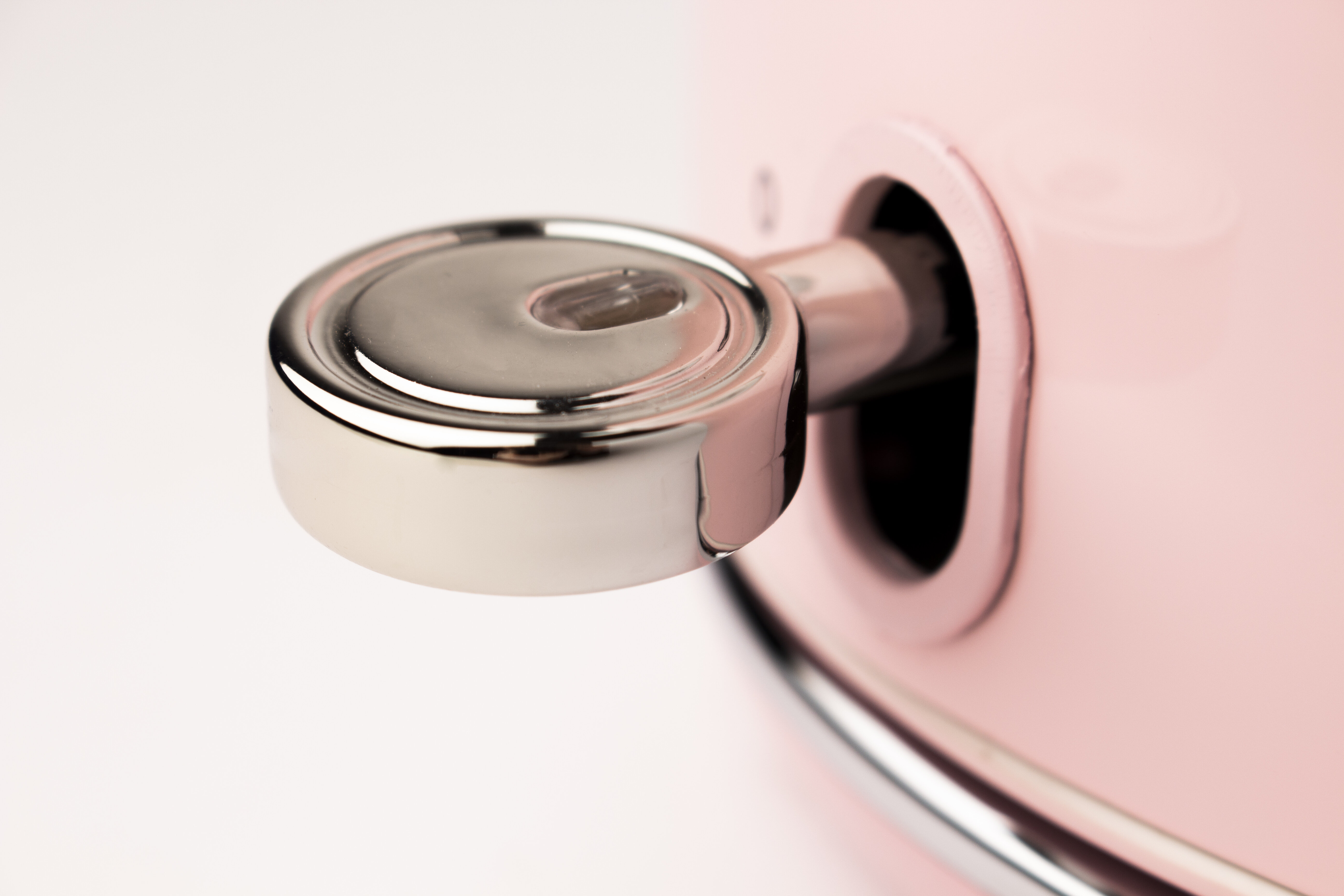 Zbliżenie włącznika/wyłącznika na różowym czajniku, ze chromowanymi detalami.