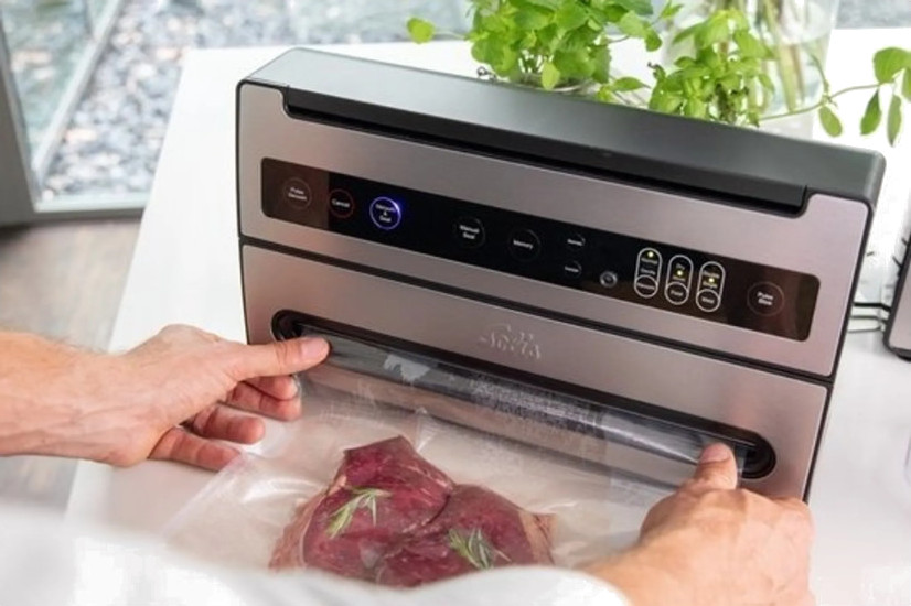 Dłonie zamykające worek próżniowy z mięsem w środku za pomocą zgrzewarki próżniowej na białym stole.