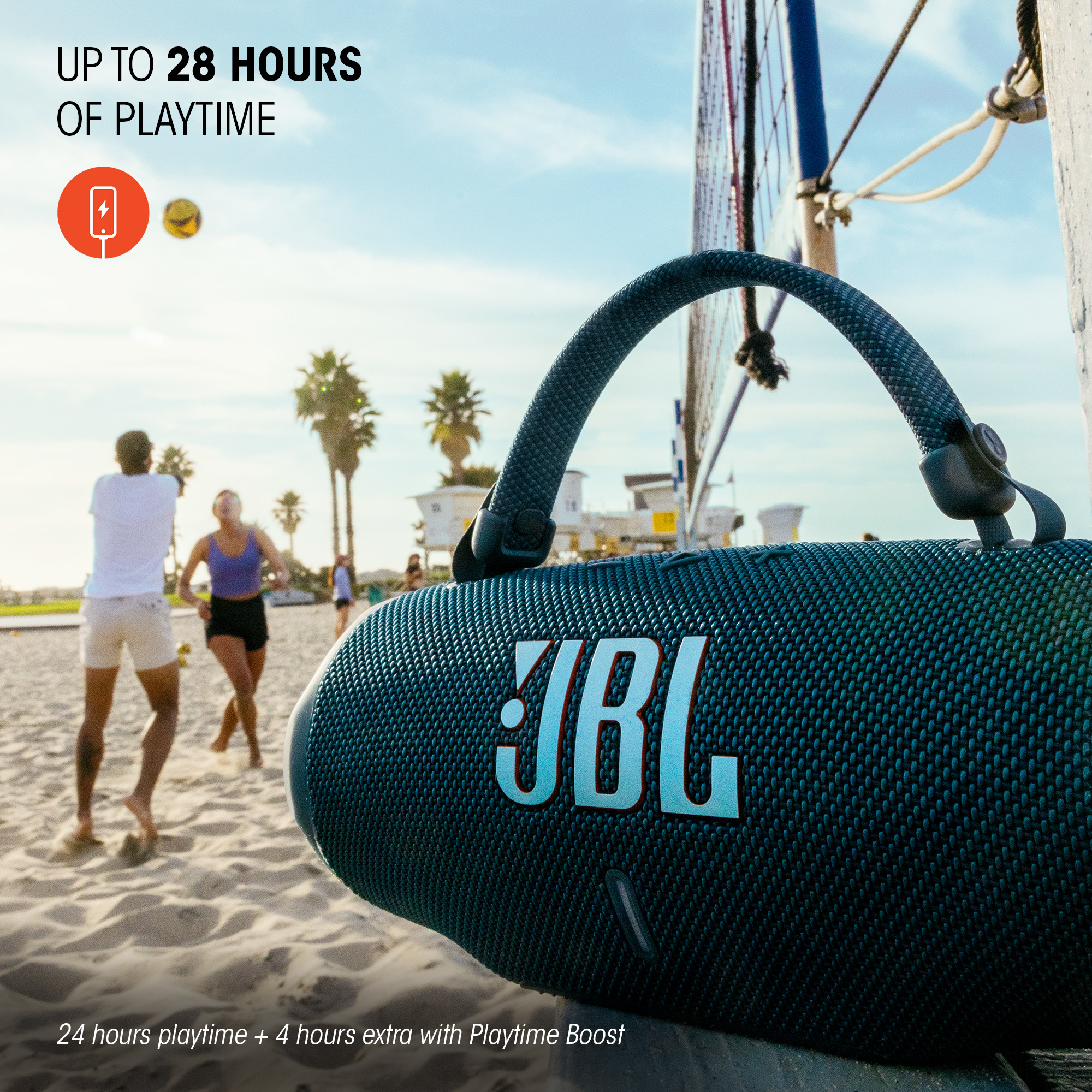 Haut-parleur JBL noir sur une plage. Deux personnes jouent en arrière-plan. La scène est en extérieur.