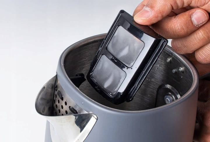Ręka wyjmująca filtr z czajnika. Filtr jest czarny.