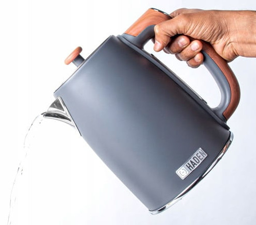 Szary czajnik z drewnianymi akcentami jest przechylony, wylewając wodę. Czajnik jest oznaczony "Haden".